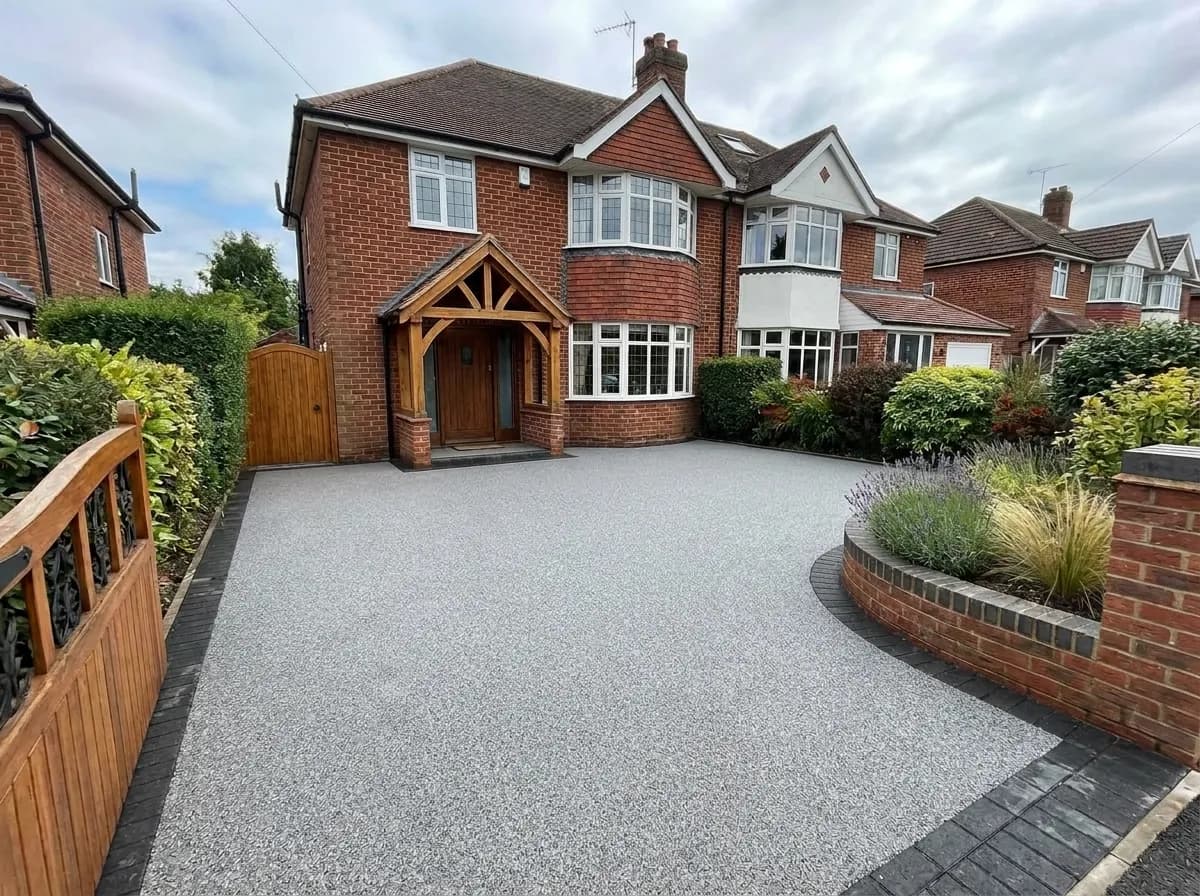 A large red brick detached house with a newly installed grey resin bound driveway, a wooden porch, and a wooden gate.